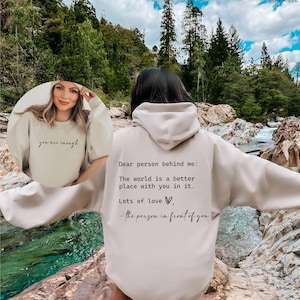 May include: A beige hooded sweatshirt with the text "Dear person behind me: The world is a better place with you in it. Lots of love, - the person in front of you" printed on the back.