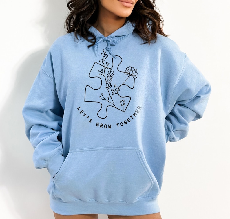 May include: Light blue hoodie with a black graphic of a puzzle piece with flowers and the text "Let's Grow Together".