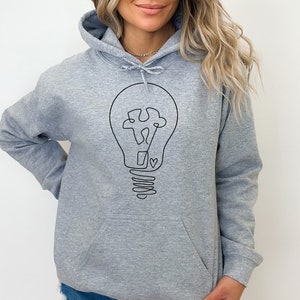 May include: A gray hooded sweatshirt with a black line drawing of a lightbulb with a heart in the center. The lightbulb is drawn in a simple, minimalist style.