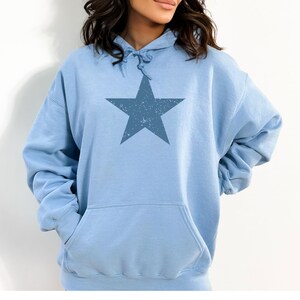 May include: A light blue hoodie with a large, distressed blue star graphic on the front. The hoodie has a drawstring hood and a kangaroo pocket.