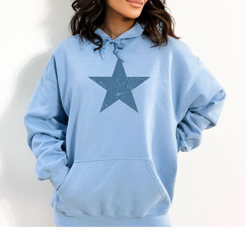May include: A light blue hoodie with a large, distressed blue star graphic on the front. The hoodie has a drawstring hood and a kangaroo pocket.