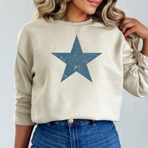 May include: A light beige sweatshirt with a distressed blue star graphic.