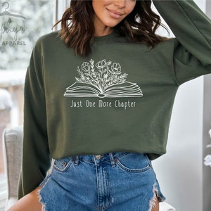 Peut inclure: Un sweat-shirt vert avec un imprim&eacute; blanc d'un livre ouvert avec des fleurs qui en sortent. Le texte "Just One More Chapter" est sous le livre.