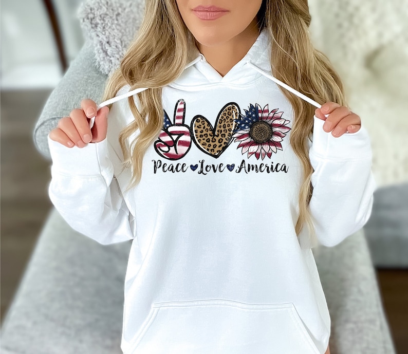 May include: White hoodie with a peace sign, heart, and sunflower graphic. The graphic features an American flag design and the text "Peace Love America".