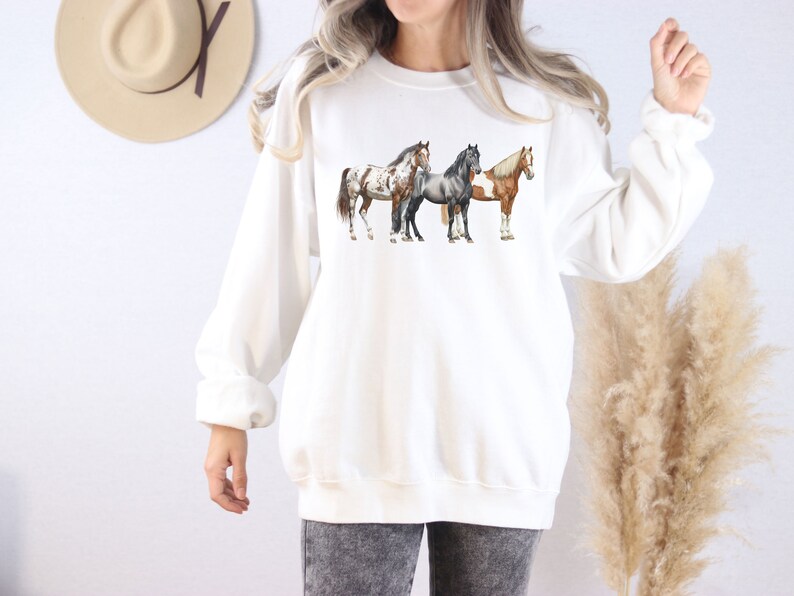 May include: White sweatshirt with a graphic of three horses in a row. The horses are brown, black, and white.