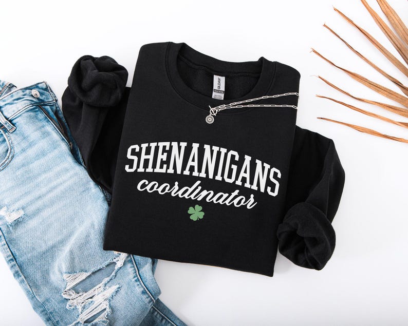 May include: Black sweatshirt with white text that reads "Shenanigans coordinator" and a green four-leaf clover.