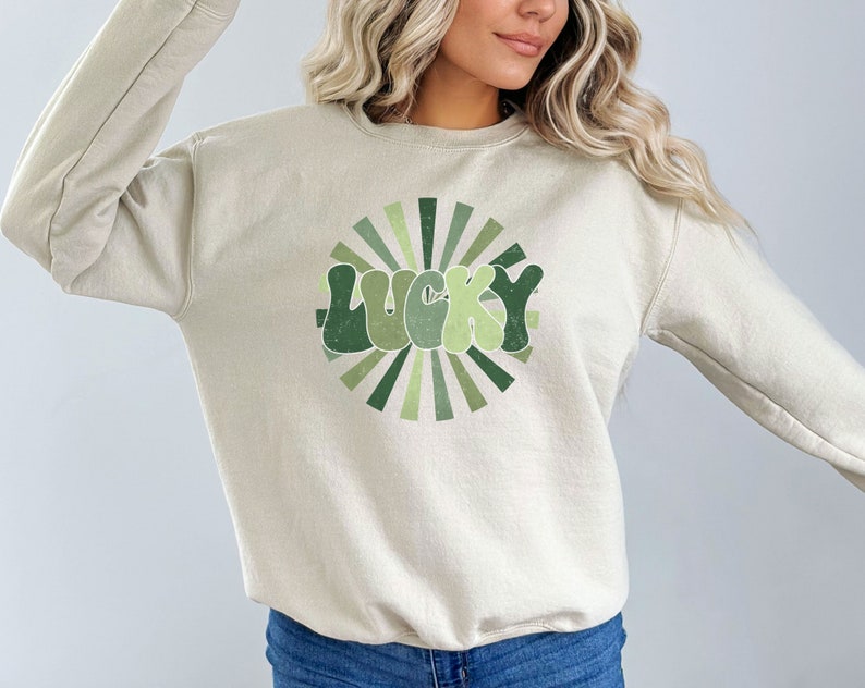Peut inclure: Un sweat-shirt beige clair avec un motif r&eacute;tro vert et blanc qui dit "LUCKY" dans un design en forme de soleil.