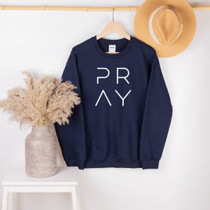 May include: Navy blue sweatshirt with the word "PRAY" printed in white on the front.