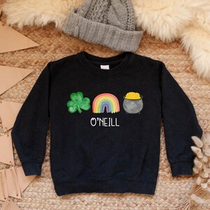 May include: Black sweatshirt with a green shamrock, rainbow, and pot of gold graphic. The text "O'NEILL" is printed below the graphic.