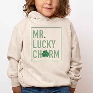 May include: A beige hoodie with a green four-leaf clover graphic and the text "MR. LUCKY CHARM" in a white box.