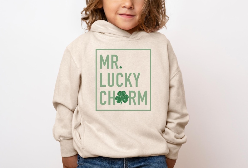 May include: A beige hoodie with a green four-leaf clover graphic and the text "MR. LUCKY CHARM" in a white box.