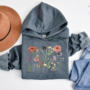 May include: A dark gray hooded sweatshirt with a floral print featuring a butterfly, flowers, and leaves. The print is in shades of pink, red, yellow, and green.