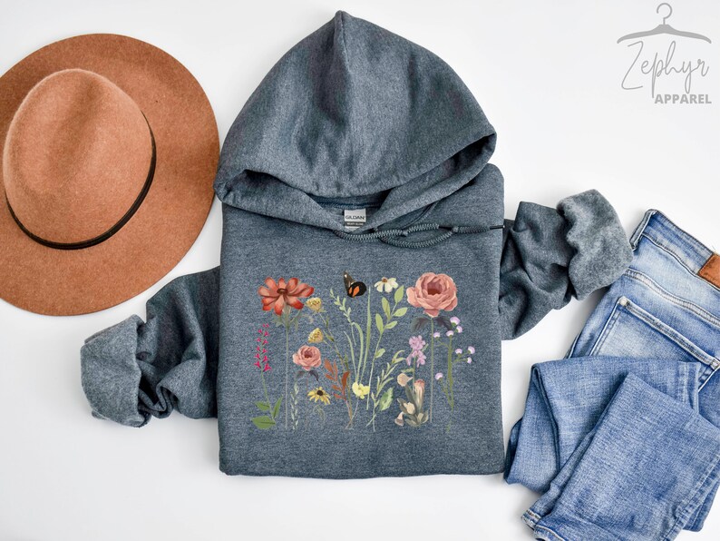 May include: A dark gray hooded sweatshirt with a floral print featuring a butterfly, flowers, and leaves. The print is in shades of pink, red, yellow, and green.