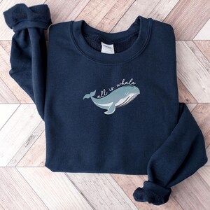 May include: A navy blue sweatshirt with a whale graphic and the text "all is whale" in white.