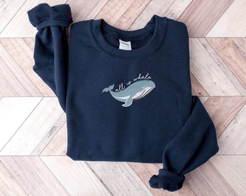 May include: A navy blue sweatshirt with a whale graphic and the text "all is whale" in white.