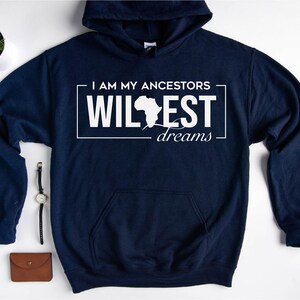 May include: Navy blue hooded sweatshirt with white text that reads "I am my ancestors wildest dreams" with an outline of the continent of Africa.