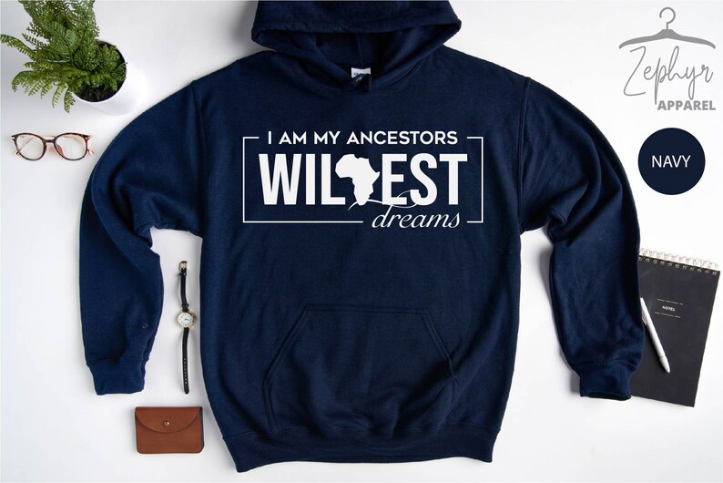 May include: Navy blue hooded sweatshirt with white text that reads "I am my ancestors wildest dreams" with an outline of the continent of Africa.