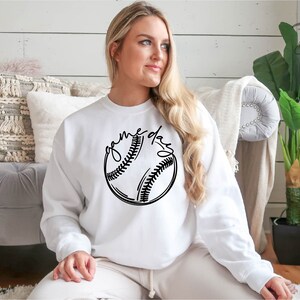 May include: White sweatshirt with a black baseball graphic and the text "game day" printed on the front.