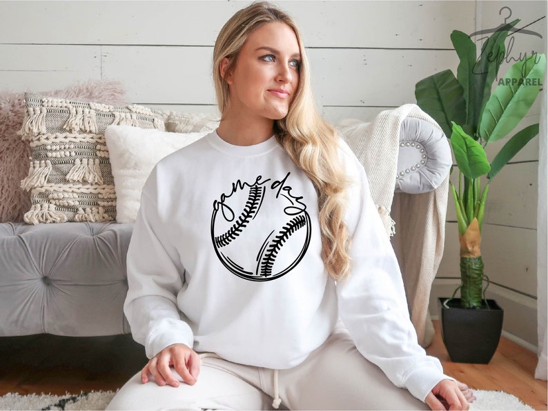 May include: White sweatshirt with a black baseball graphic and the text "game day" printed on the front.
