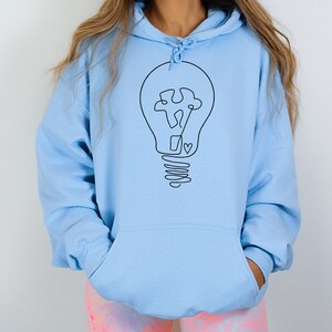May include: A light blue hoodie with a black outline of a lightbulb with a puzzle piece inside. The lightbulb has a heart at the bottom of the base.