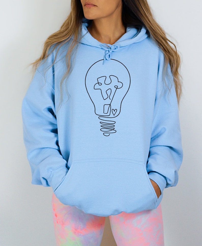 May include: A light blue hoodie with a black outline of a lightbulb with a puzzle piece inside. The lightbulb has a heart at the bottom of the base.
