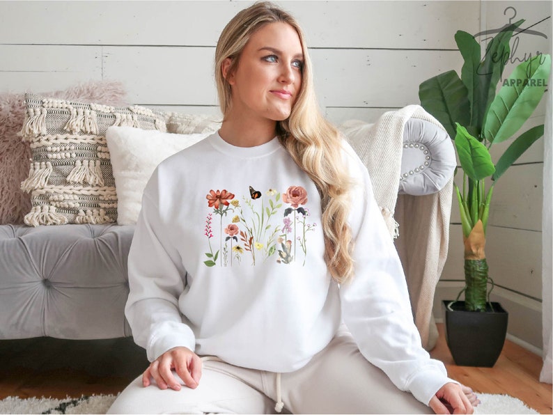 May include: White sweatshirt with a floral print featuring a butterfly, red, pink, and yellow flowers, and green leaves.