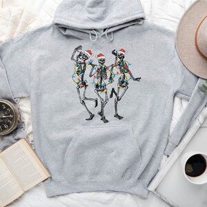 May include: A gray hooded sweatshirt with a graphic of three skeletons wearing Santa hats and Christmas lights. The skeletons are dancing.