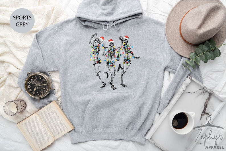 May include: A gray hooded sweatshirt with a graphic of three skeletons wearing Santa hats and Christmas lights. The skeletons are dancing.