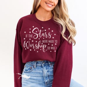 May include: Burgundy sweatshirt with the text "If the Stars Were Made to Worship So Will I" in white script. The design includes stars around the text. The sweatshirt is a long-sleeved crew neck.