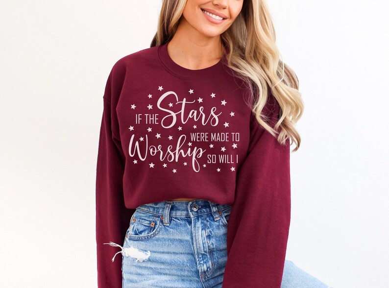 May include: Burgundy sweatshirt with the text "If the Stars Were Made to Worship So Will I" in white script. The design includes stars around the text. The sweatshirt is a long-sleeved crew neck.