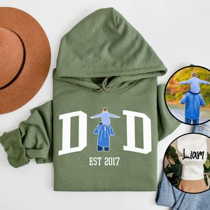 May include: Green hooded sweatshirt with white text that reads "DAD EST 2017" and a graphic of a father carrying a child on his shoulders. The sweatshirt has a white cuff with the name "Liam" embroidered on it.