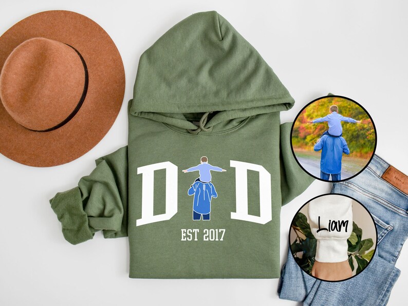 May include: Green hooded sweatshirt with white text that reads "DAD EST 2017" and a graphic of a father carrying a child on his shoulders. The sweatshirt has a white cuff with the name "Liam" embroidered on it.
