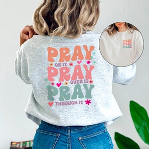 May include: A grey sweatshirt with a colourful graphic on the back that says "Pray on it, Pray over it, Pray through it".