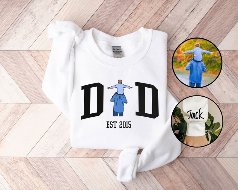 May include: White sweatshirt with a black graphic of a father carrying a child on his shoulders. The graphic says "DAD EST 2015".