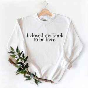 May include: White sweatshirt with the text "I closed my book to be here."