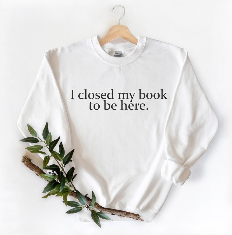 May include: White sweatshirt with the text "I closed my book to be here."