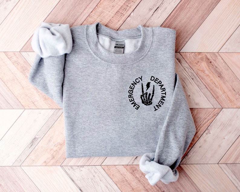 May include: Gray sweatshirt with a black graphic of a skeleton hand making a rock and roll sign with a lightning bolt. The graphic is inside a circle with the words "Emergency Department" around it.