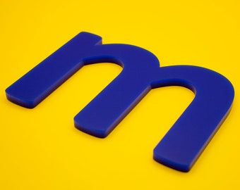 May include: A blue plastic letter M on a yellow background.