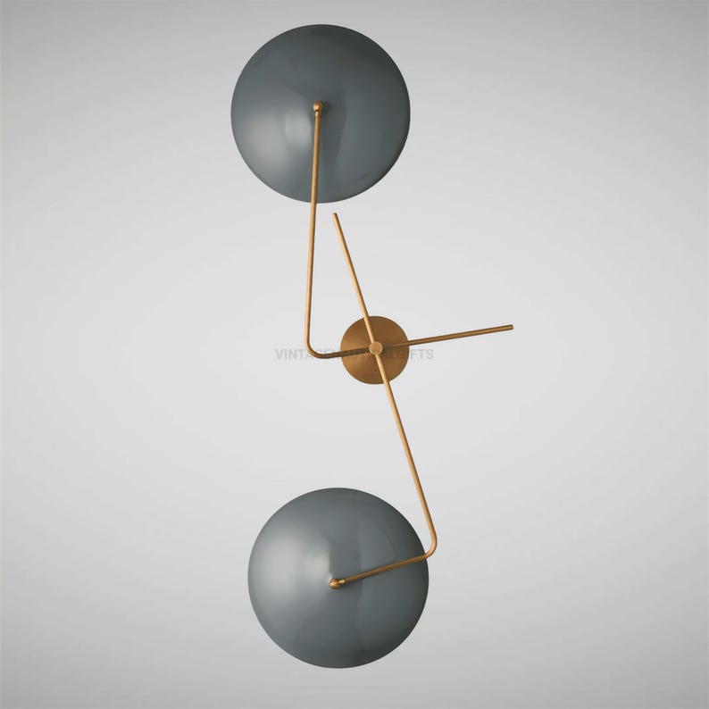 May include: A modern wall-mounted light fixture with two round, gray shades and gold metal arms. The fixture has a minimalist design and would add a touch of contemporary style to any room.