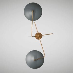 May include: A modern wall-mounted light fixture with two round, gray shades and gold metal arms. The fixture has a minimalist design and would add a touch of contemporary style to any room.