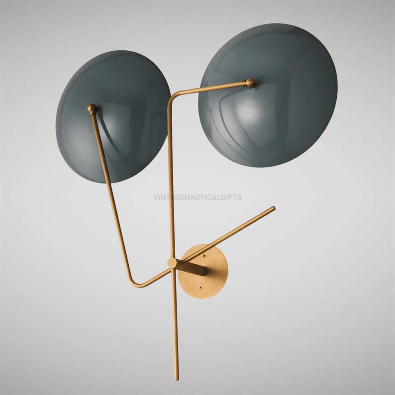 May include: A modern wall sconce with two round, gray metal shades and a gold metal frame. The shades are angled outward and the frame is attached to the wall with a round, gold metal plate.