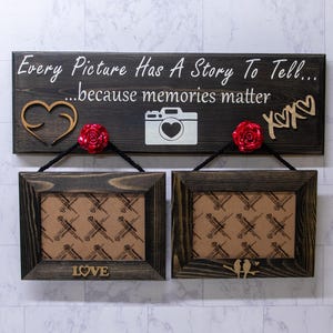 May include: A wooden sign with the text "Every Picture Has A Story To Tell... ...because memories matter" with two picture frames hanging below. The sign has a gold heart, a camera, and two red roses.