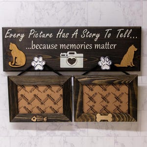 May include: A wooden sign with the text "Every Picture Has A Story To Tell... ...because memories matter". The sign has two photo frames with a paw print and a camera cutout on each side. The frames are brown and have a white background.