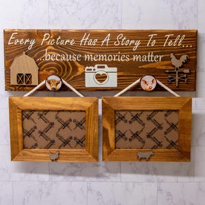 May include: Wooden sign with the text "Every Picture Has A Story To Tell... because memories matter". The sign has a barn, camera, pig, and rooster cutout. Two brown picture frames hang below the sign.