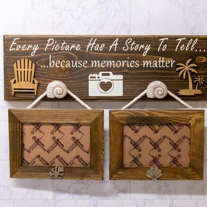 May include: A wooden sign with the text "Every Picture Has A Story To Tell... because memories matter."  The sign has a camera, seashells, and palm trees carved into it. Two wooden picture frames hang below the sign.