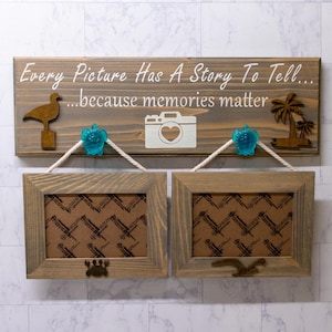 May include: A wooden sign with the text "Every Picture Has A Story To Tell... because memories matter" with a seagull, a camera, and a palm tree. Two wooden picture frames are hanging below the sign.