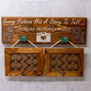 May include: Wooden photo frame with two picture slots. The top board has the text "Every Picture Has A Story To Tell...because memories matter". It features a camera graphic, sunflower cutouts, and green butterfly accents. The frames are connected by rope.