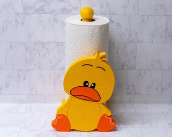 May include: Yellow wooden duck paper towel holder with orange feet and a white paper towel roll.