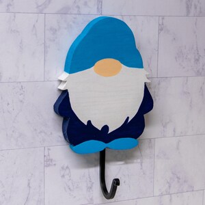 May include: A blue and white gnome-shaped wooden hook with a black metal hook. The gnome has a blue hat, a white beard, and a light orange nose.