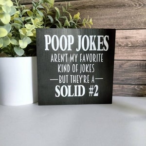 May include: Black wooden sign with white text that reads "Poop Jokes Aren't My Favorite Kind Of Jokes - But They're A Solid #2".